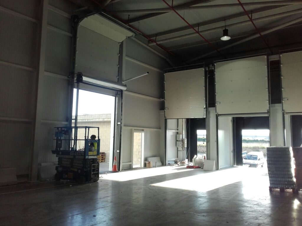 Interior de nave con acceso de camiones y puertas seccionales elevadas.